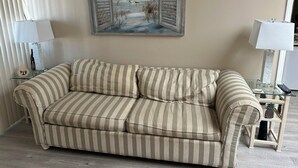 A striped sofa in a room with a painting of a beach scene on the wall.