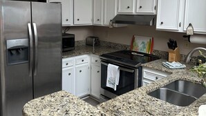 A modern kitchen with white cabinets, stainless steel appliances, granite countertops, and a granite backsplash.