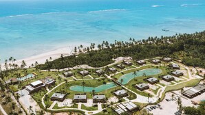 Vue aérienne d’un complexe hôtelier comprenant plusieurs bâtiments, des piscines et une plage.