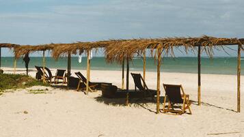 Una playa con sombrillas de paja y sillones de descanso.