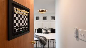 A bedroom with a chessboard, a bed with black and white bedding, a ceiling light, and framed artwork on the wall.