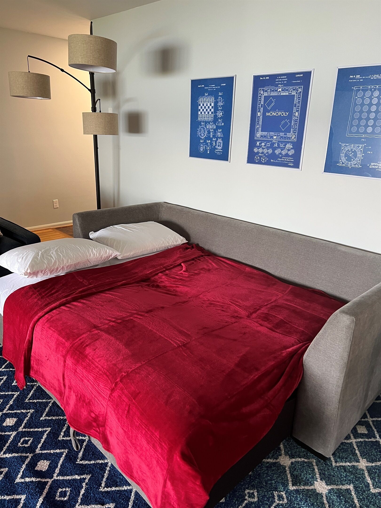 Une chambre moderne avec un canapé-lit gris, une couverture rouge et un tapis bleu à motifs.