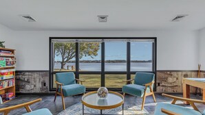 A room with large windows, two blue chairs, a round table, and a bookshelf.