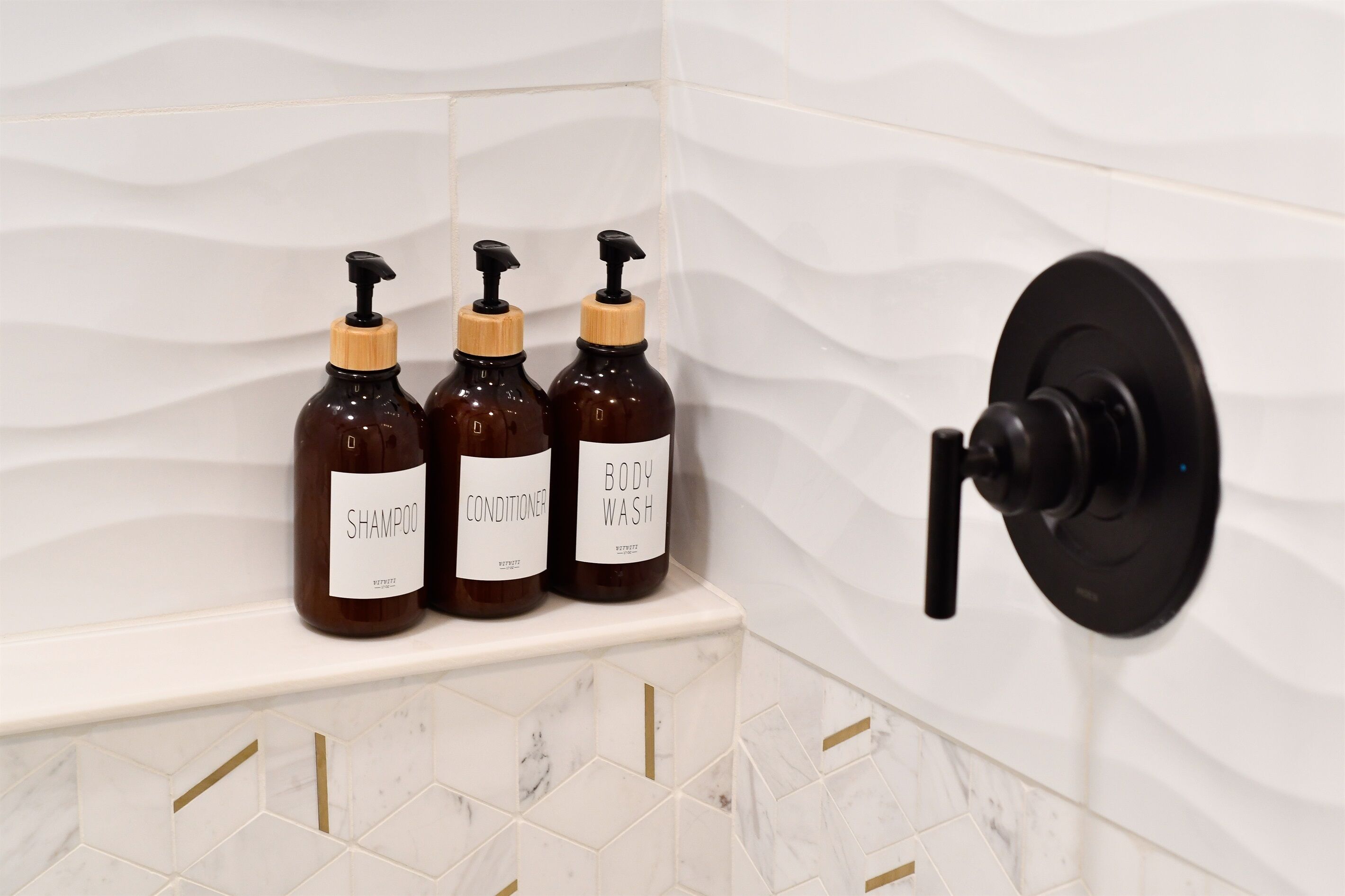 Casa de banho com três frascos de champô, condicionador e gel de banho numa prateleira.