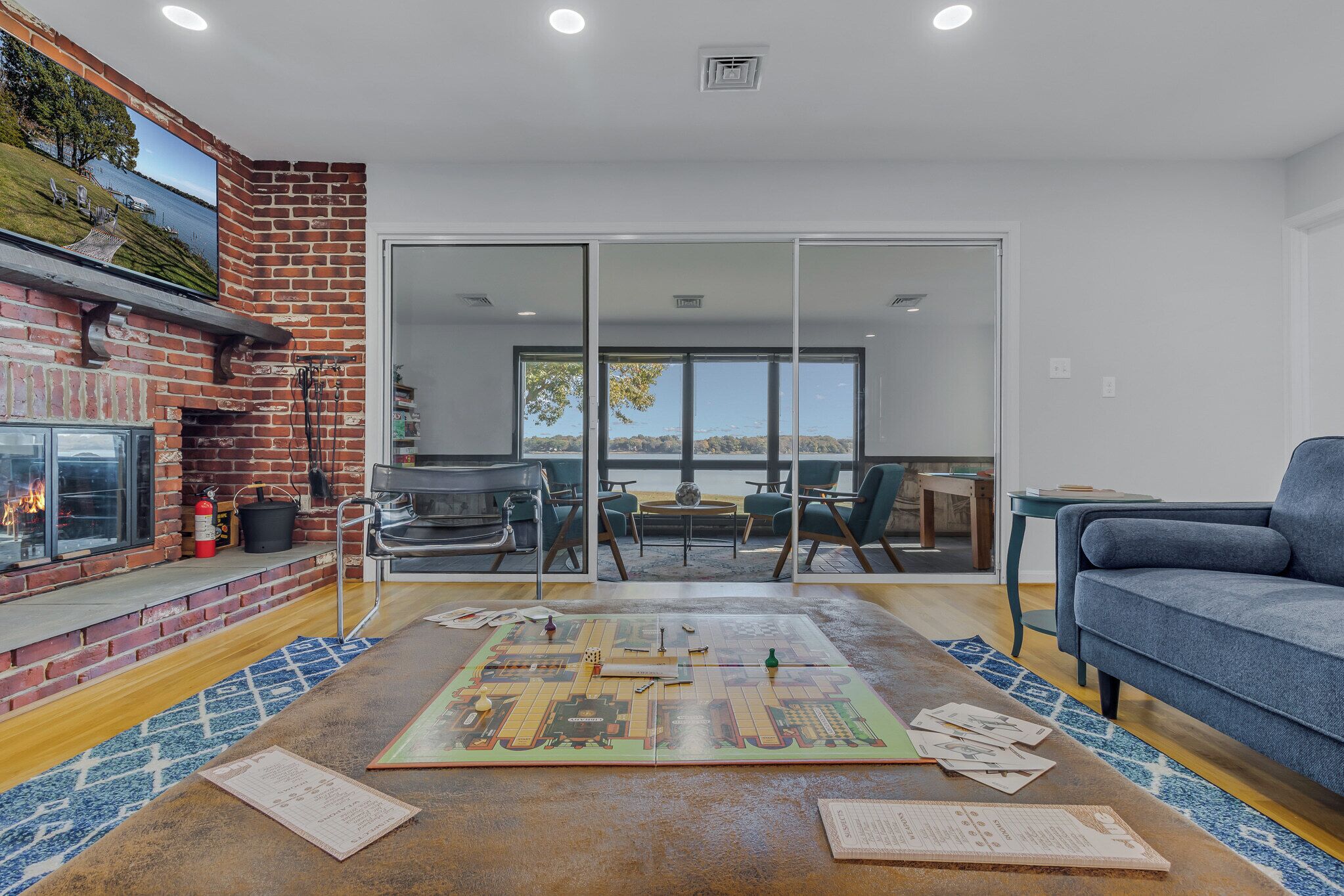Una sala de estar con chimenea de ladrillo, un ventanal grande, un sofá azul y una mesa de centro con juegos de mesa.