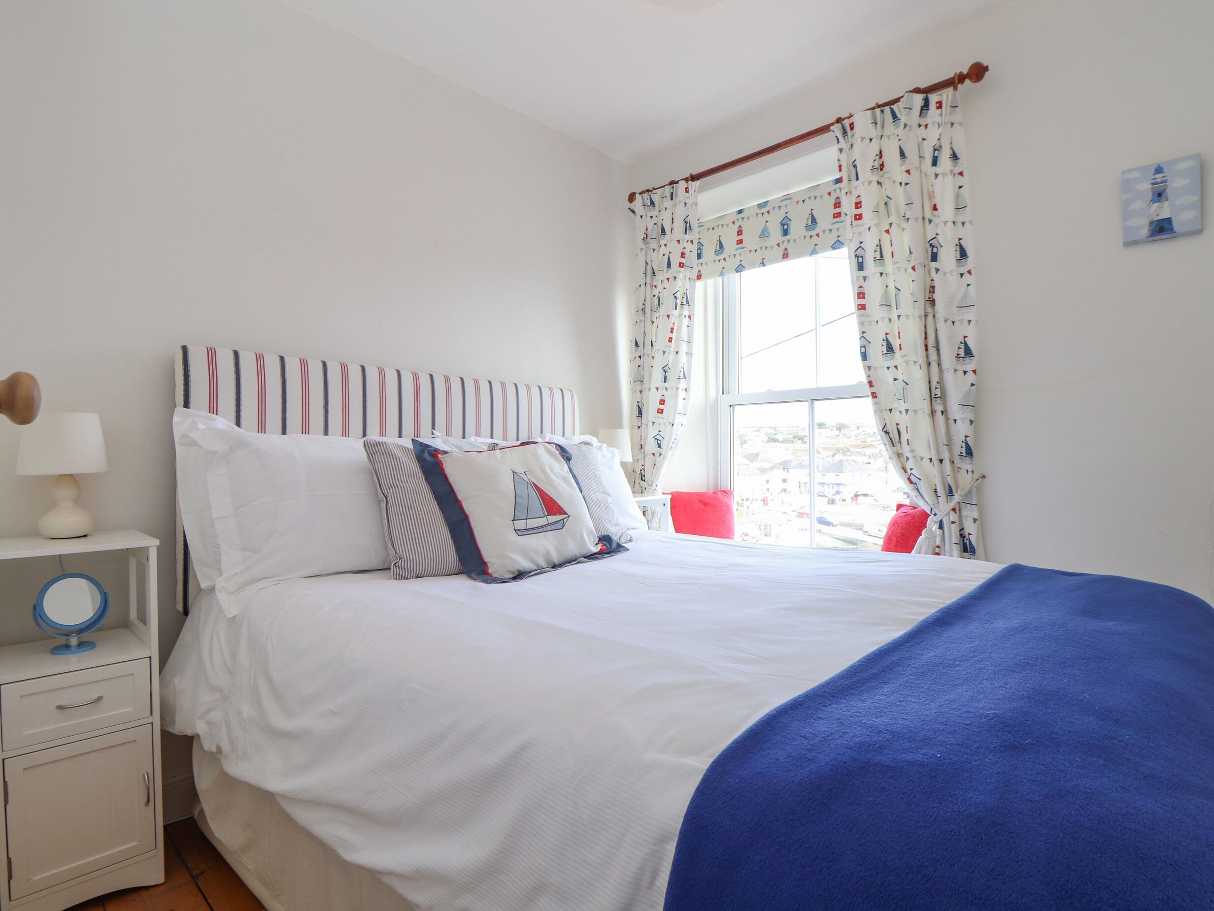 A bedroom with a bed, a nightstand, a lamp, a mirror, and a window with curtains.