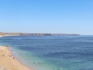 A coastal beach with clear blue waters, sandy shore, and rocky cliffs in the background. - Crab Pot Cottage (Helston)