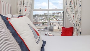 Quarto com uma grande janela, roupa de cama listrada e cortinas com tema náutico.