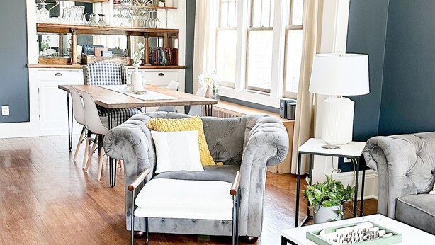 Ein modernes Wohnzimmer mit einem grauen Sofa, einem Esstisch und einer Küche im Hintergrund.