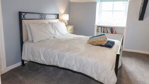 Una cama bien hecha con ropa blanca, una lámpara de noche y una ventana con vistas al exterior.