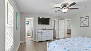 Ein Schlafzimmer mit einem Bett, einem Deckenventilator, einer Kommode und einem Fernseher.