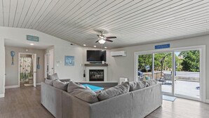 Ein modernes Wohnzimmer mit einem grauen Ecksofa, einem Deckenventilator, einem Flachbildfernseher und einem Kamin.