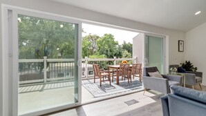 Ein modernes Wohnzimmer mit Glastür zum Balkon, einer Couch, einem Couchtisch und einem Essbereich mit Stühlen und Tisch.