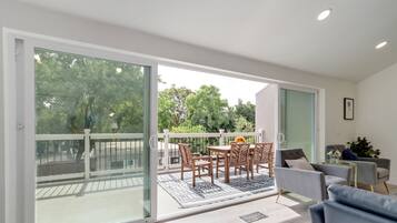 A modern living room with a glass door leading to a balcony, a sofa, a coffee table, and a dining area with chairs and a table.