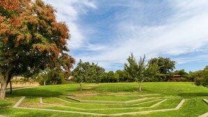 Ein Park mit geometrisch angelegtem Rasen, Bäumen und blauem Himmel.