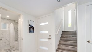 Ein modernes Interieur mit einer Marmordusche, einer Treppe mit Holzvertäfelung und einer weißen Tür mit gebürstetem Glas.