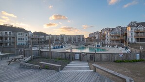A waterfront residential area with a swimming pool, wooden deck, and multiple apartment buildings. - 2910 - Dolphin's Den, Duck Condo | Pools, Tennis & Views (Duck)