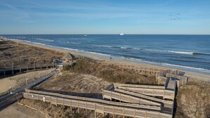 A beach with wooden boardwalks, a pier, and a sailboat in the distance. - 2910 - Dolphin's Den, Duck Condo | Pools, Tennis & Views (Duck)