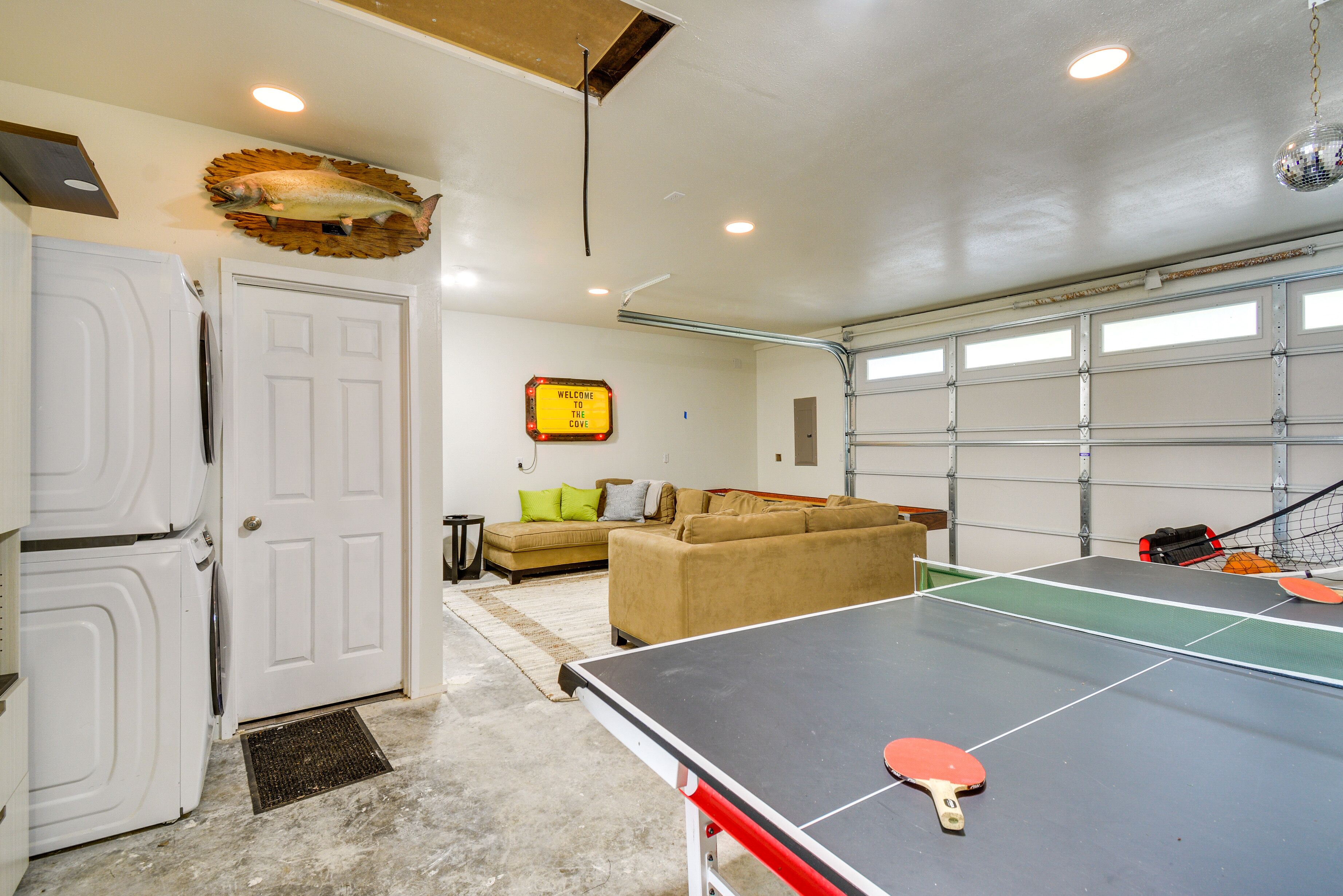 Una habitación con mesa de ping pong, una puerta blanca, un sofá y una puerta de garaje.