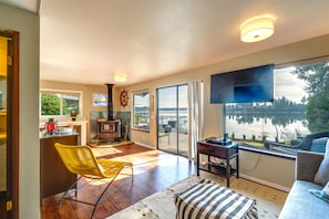 A spacious living area with a large window overlooking a lake, a fireplace, and a television mounted on the wall.