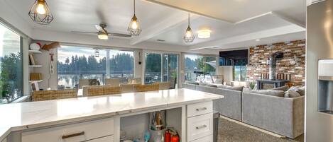 A modern kitchen with a large island, white cabinetry, and pendant lighting. There are wicker baskets on the island, and a fire extinguisher is visible.