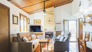 A spacious living room with a fireplace, a ceiling fan, and a television. - Cubo's Casa Rural Jose & Caminito del Rey / Piscina privada / Caminito del Rey (Ardales)
