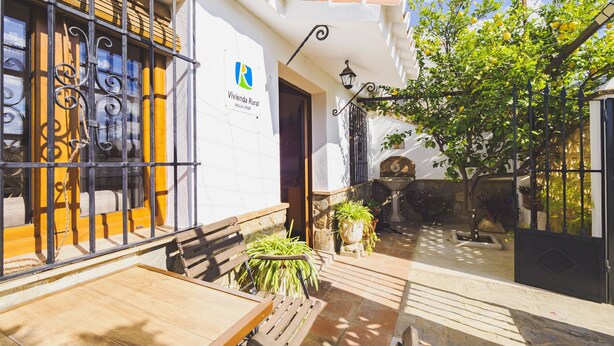 A patio area with a wooden table and chairs, a stone fountain, and a potted plant. - Cubo's Casa Rural Jose & Caminito del Rey / Piscina privada / Caminito del Rey (Ardales)