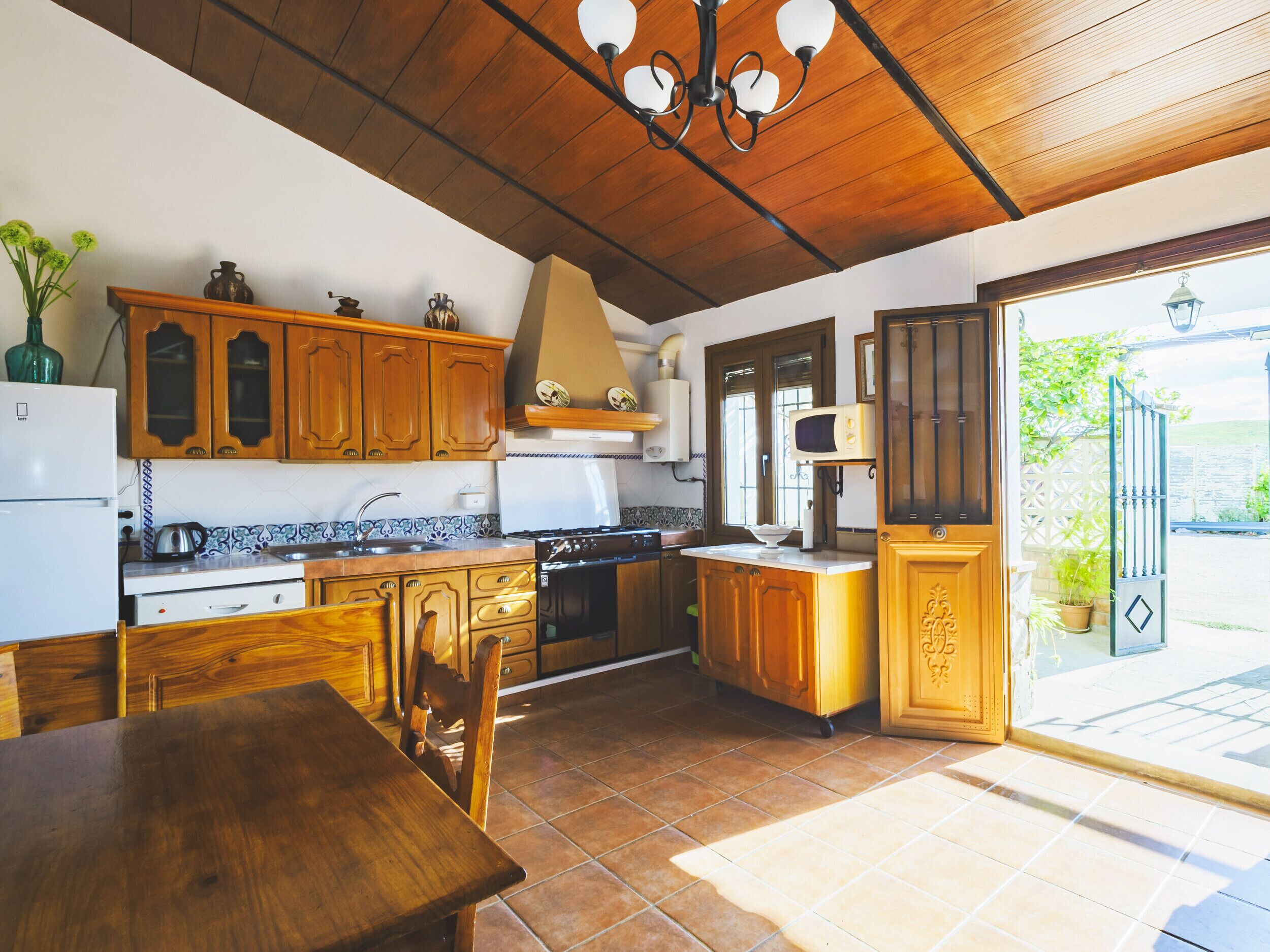 Een keuken met houten kastjes, een fornuis en een eethoek met een tafel en stoelen.