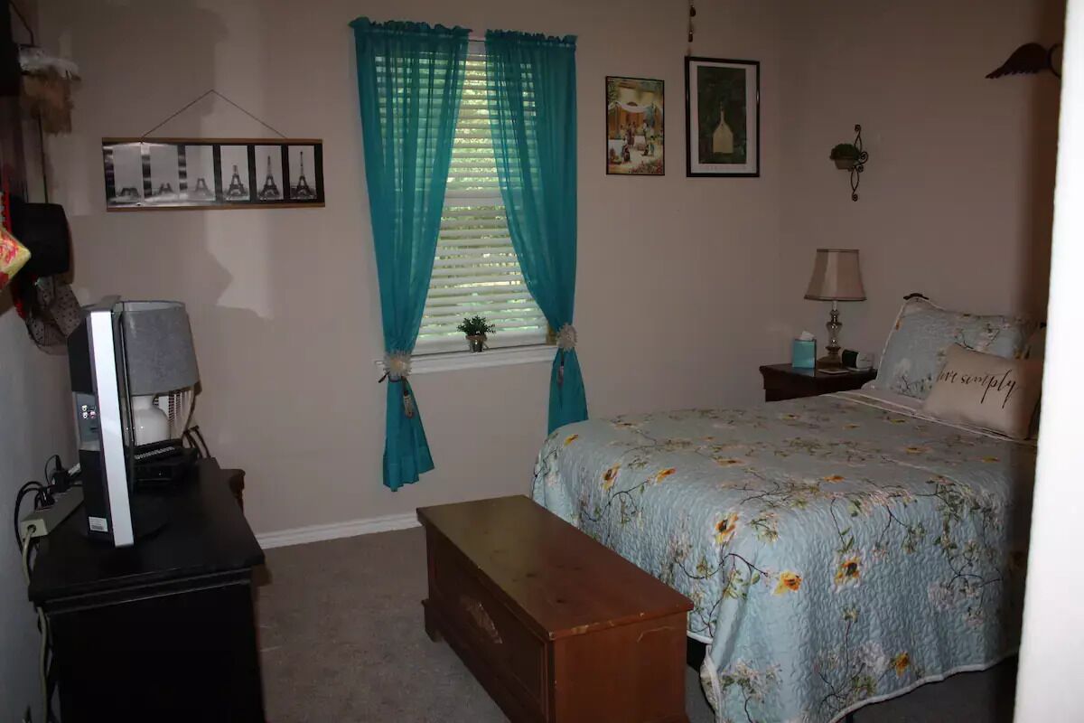 A bedroom with a bed, a desk with a computer, a window with curtains, and wall decorations.