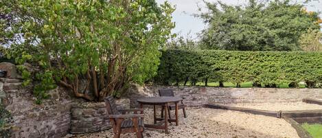 Un espace patio agrémenté d’un mur en pierre, d’une table et d’une chaise en bois, et d’un grand arbre.