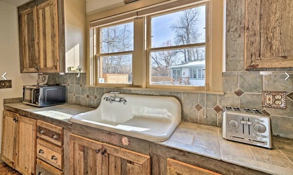 A kitchen with a large sink, wooden cabinets, a window with a view of a house, and a toaster.