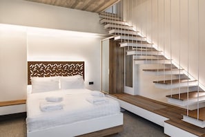 Una habitación de hotel moderna con una cama grande, cabecera de madera, una escalera integrada y vistas al exterior.