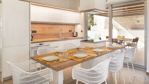 A modern kitchen with white cabinets, a wooden countertop, and a dining area with white chairs and a table set for four.