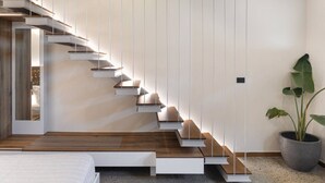 A modern staircase with wooden steps and white walls, leading to a bedroom with a bed and a potted plant.
