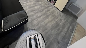 Ett modernt vardagsrum med en stor platt-TV, en svart soffa och en matplats med stolar och ett bord.