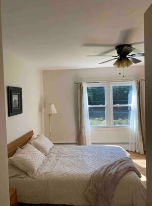 A bedroom with a bed, a ceiling fan, a window with curtains, and a floor lamp.