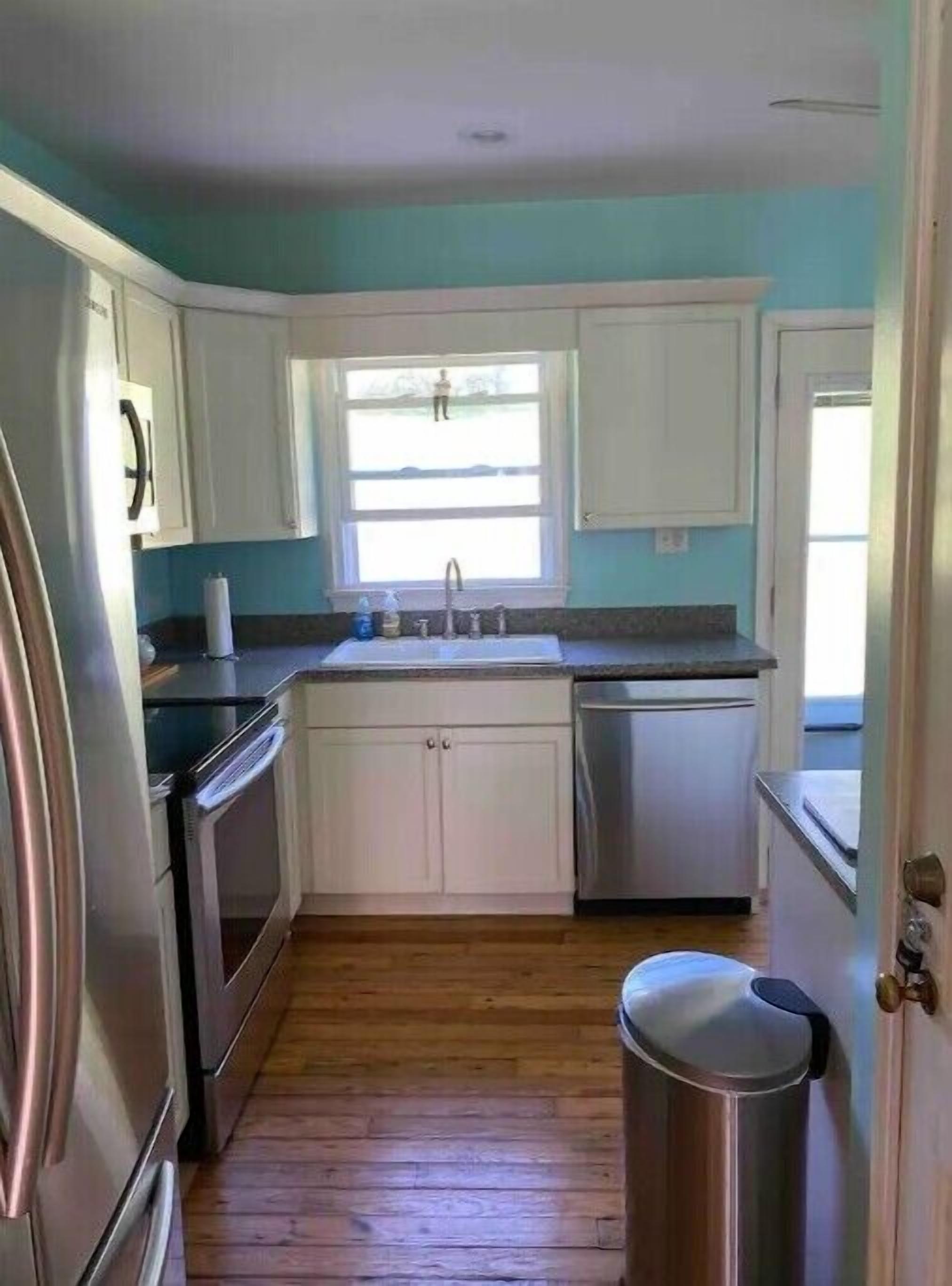 A kitchen with white cabinets, stainless steel appliances, a window with a view, and a trash can.