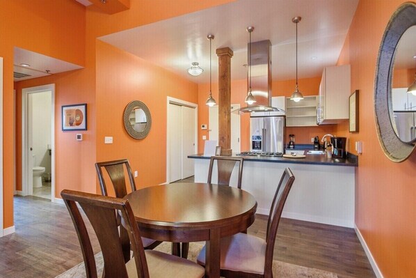 Un comedor con mesa y sillas de madera, una cocina con refrigerador y estufa, y paredes color naranja.