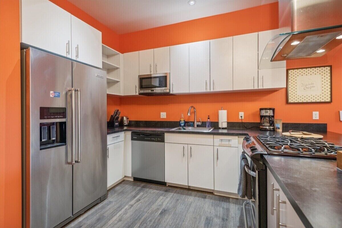 A modern kitchen with stainless steel appliances, white cabinets, and an orange accent wall.