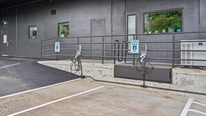 A parking area with electric vehicle charging stations, a reserved parking sign, and a building with windows and a door. - Quiet End-Unit Studio w/ Full Kitchen + Natural Light (Portland)