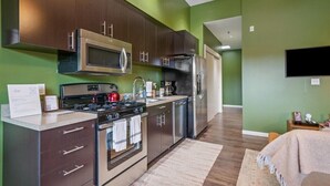 A modern kitchen with dark cabinets, stainless steel appliances, and a green accent wall. - Quiet End-Unit Studio w/ Full Kitchen + Natural Light (Portland)