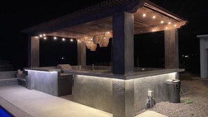 Un espace bar extérieur doté d’une pergola, de sièges et d’une piscine.