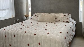 Une chambre à coucher comprenant un lit, un ventilateur de plafond, une fenêtre avec des rideaux et un mur à la finition texturée.