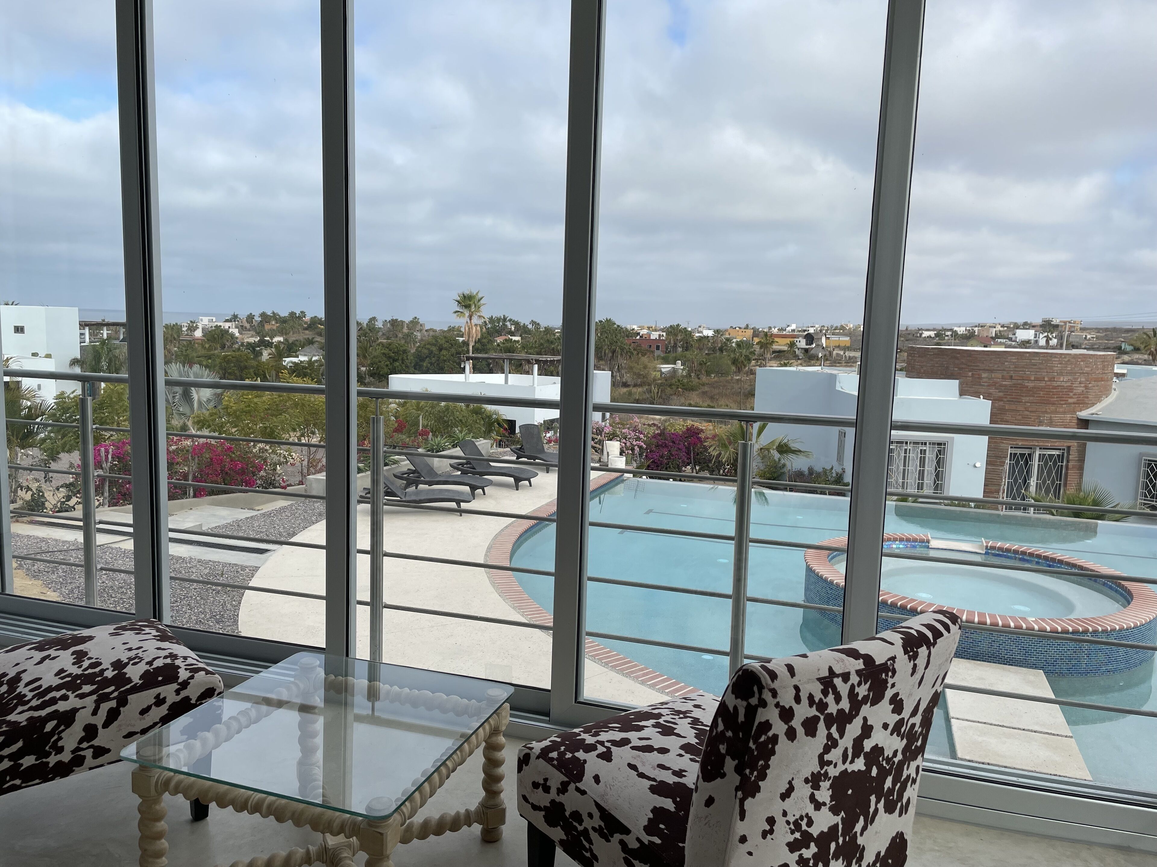 A view from a balcony with a pool, lounge chairs, and a glass table.