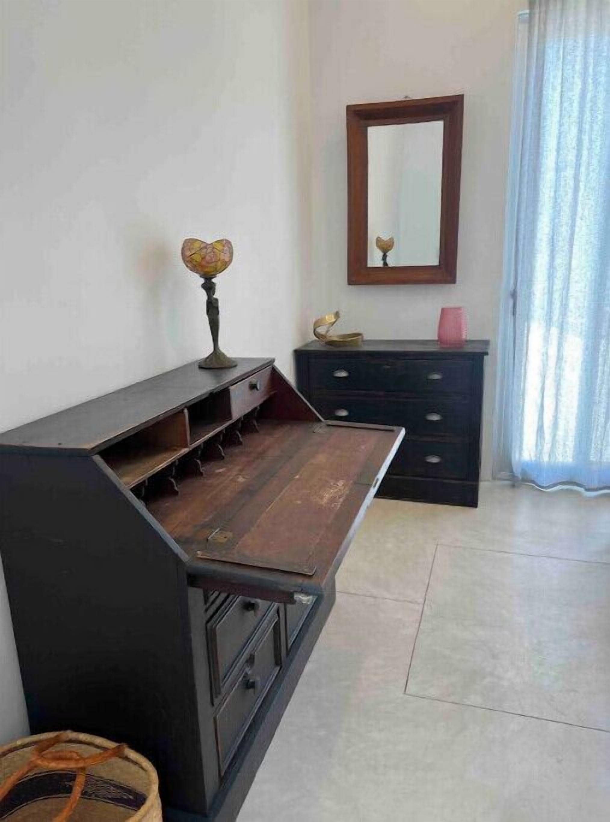 A room with a dark wooden bench with drawers, a small globe on top, a mirror on the wall, and a pink cup on a dresser.