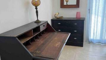 A room with a dark wooden bench with drawers, a small globe on top, a mirror on the wall, and a pink cup on a dresser.