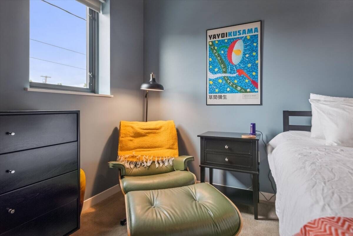 A bedroom with a bed, a green chair, a nightstand, a dresser, and a poster on the wall.