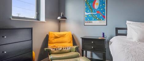A bedroom with a bed, a green chair, a nightstand, a dresser, and a poster on the wall.