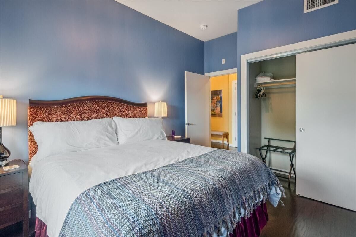 A bedroom with a bed, bedside lamps, a wardrobe, and a small table with a chair.