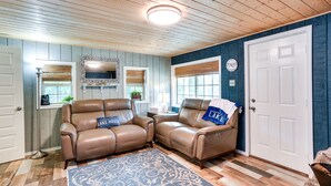 A room with two leather recliners, a patterned rug, wooden flooring, a white door, and a clock on the wall.